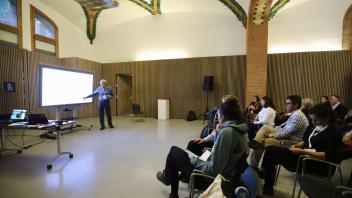 Hugh Safford in 8th Mediterranean Forest Week. A presenter pointing at a screen during a conference in a room with wooden paneling and decorative ceiling patterns.