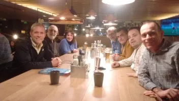 Group of seven people sitting at a long table in a warmly lit restaurant or bar.