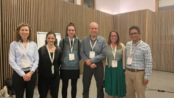 A group of six people standing indoors in front of wooden paneling in the Mediterranean Forest Week