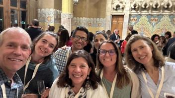 A group of seven people smiling at an indoor event with ornate architecture in the background.