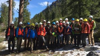 A group of people wearing hard hats and safety vests standing in a snowy forest.