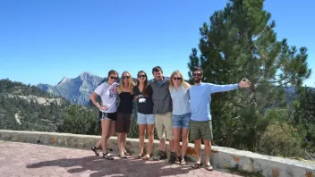 Group of six people standing together with a mountain view.