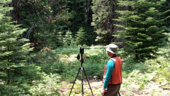 Person with a Lidar in a tripod in a forested area.