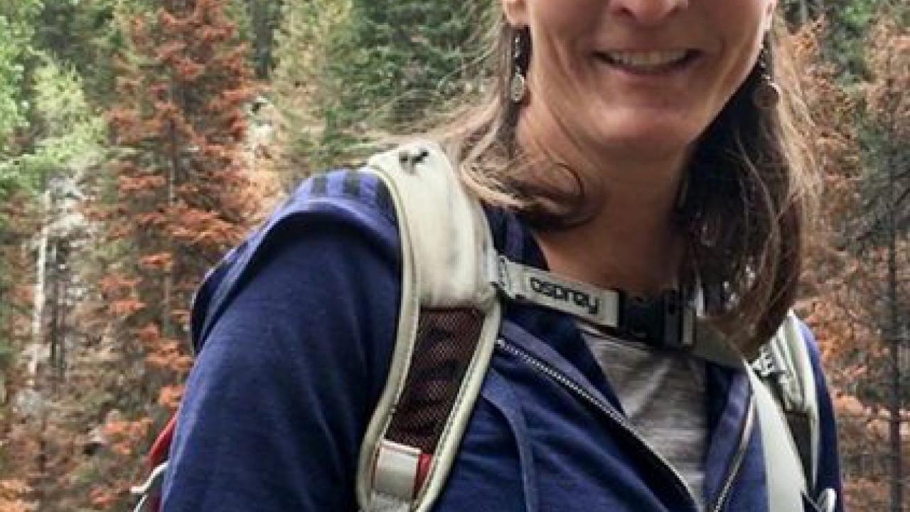 Person in outdoor attire with a mountain forest backdrop.