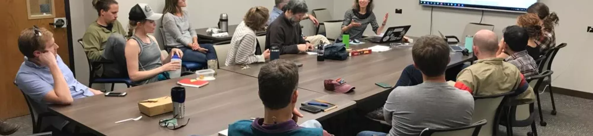 People sitting around a conference table in a meeting room with a monitor displaying an image of a wildfire.