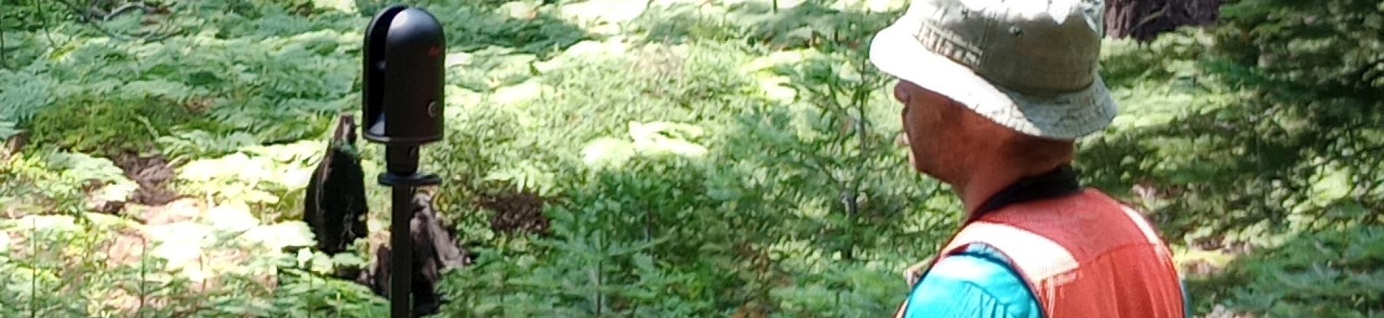 A person in a forested area using a terrestrial lidar in a tripod